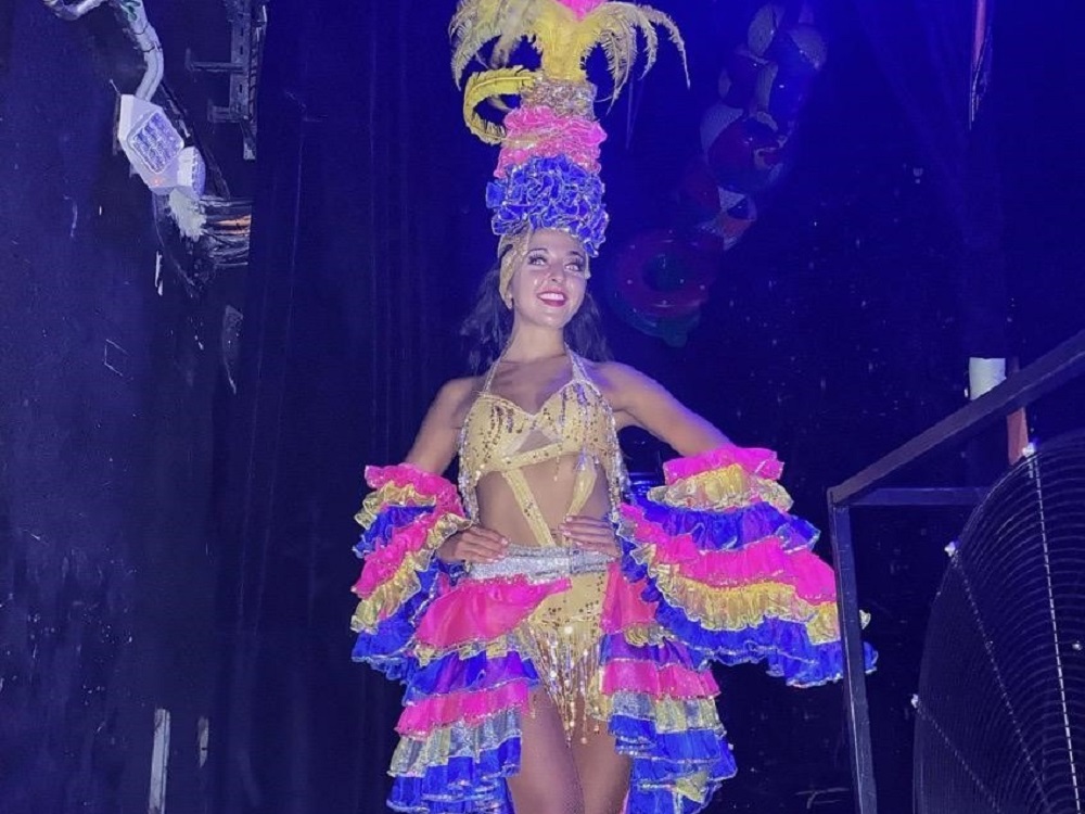 Photo of a young woman in a flamboyant costume, preparing to dance on stage.